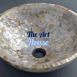 May include: Oval-shaped bathroom sink with a mosaic design. The sink is made of small, iridescent tiles in shades of white, beige, and gold. The text "The Art House" is displayed in the center of the sink.