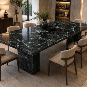 Peut inclure: Une table à manger rectangulaire dotée d'un plateau en marbre noir poli avec des veines blanches et d'un pied central assorti. La table est entourée de huit chaises avec des cadres en bois foncé, des assises beiges et des dossiers incurvés.