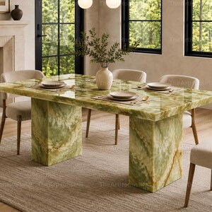 May include: A rectangular dining table featuring a polished green onyx surface with natural veining and two thick, matching pedestal bases. The table is surrounded by four upholstered chairs with light beige fabric and wooden legs.