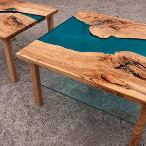 May include: Two wooden side tables with a live edge design and teal epoxy resin inlays. The tables have natural wood grain and are supported by four wooden legs. The tables are approximately 24 inches long and 18 inches wide.