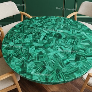Op de afbeelding: Een ronde tafel met een levendig groen malachietblad, met een mozaïekpatroon van donkere en lichtgroene tinten. De tafel wordt omringd door vier houten stoelen met beige gestoffeerde zittingen, wat een elegante eethoek creëert.