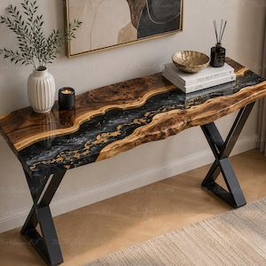 May include: A console table featuring a live edge wood slab with a central river of black and gold resin. The table has a glossy finish and is supported by two black metal X-shaped legs. The surface displays natural wood grain and knots.