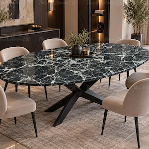 May include: An oval dining table with a black and white marble-patterned top and a black metal cross-base, surrounded by six beige upholstered chairs with black legs. A small dark vase with greenery sits in the centre of the table surface.