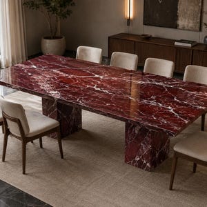 Puede incluir: Una mesa de comedor rectangular con una superficie de mármol rojo intenso pulido con vetas blancas, sostenida por dos bases de pedestal de mármol rojo a juego, rodeada de seis sillas con asientos tapizados en beige claro y marcos de madera oscura.