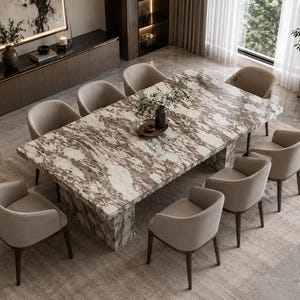 Pode incluir: Uma mesa de jantar retangular com tampo e base em mármore branco e castanho, rodeada por oito cadeiras com braços estofadas num tom bege neutro. A mesa apresenta um padrão veado proeminente e as cadeiras têm pernas de madeira escura.