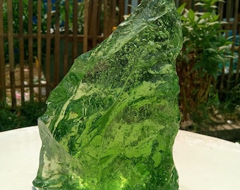 May include: A large, green, glass rock with a rough, textured surface. The rock is sitting on a white surface.