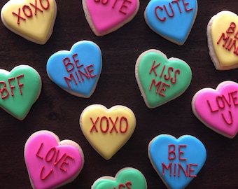 May include: A collection of heart-shaped cookies decorated with Valentine's Day messages. The cookies are in various colors, including pink, blue, yellow, and green. The messages on the cookies include "XOXO", "BFF", "Love U", "Kiss Me", "Be Mine", and "Cute".