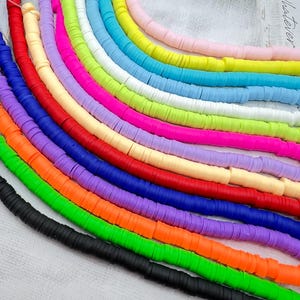 Puede incluir: Una colección de cuentas de arcilla polimérica de colores en varios tonos, incluyendo rojo, naranja, verde, azul y morado. Las cuentas son planas, en forma de disco, y están dispuestas en líneas curvas, mostrando una vibrante gama de colores. Ideales para la creación de joyas y manualidades.