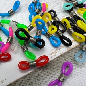 May include: Assortment of colorful plastic eyeglass chain holders with metal spring closures. The holders come in a variety of colors, including red, blue, green, yellow, black, and purple.