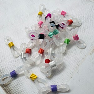 May include: A group of clear plastic eyeglass chain holders with colorful metal accents. The holders are in various colors, including red, orange, yellow, green, blue, purple, and pink.