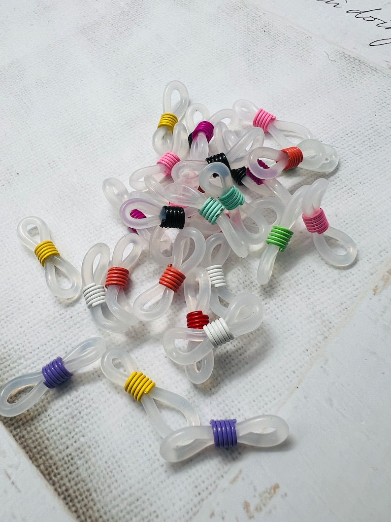 May include: A group of clear plastic eyeglass chain holders with colorful metal accents. The holders are in various colors, including red, orange, yellow, green, blue, purple, and pink.
