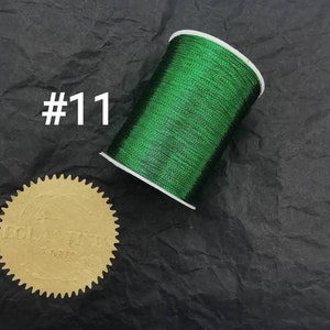 May include: A spool of green metallic thread, labelled #11, on a black textured surface.