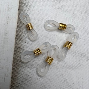 May include: Five clear plastic eyeglass holders with gold metal rings. The holders are shaped like a figure eight.