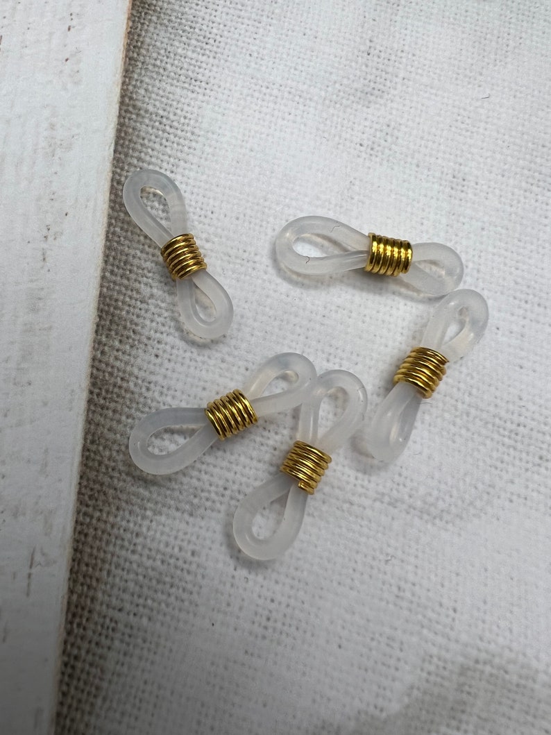 May include: Five clear plastic eyeglass holders with gold metal rings. The holders are shaped like a figure eight.