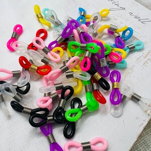 May include: Assortment of colorful plastic eyeglass chain holders with metal spring closures. The holders come in a variety of colors, including red, blue, green, yellow, pink, purple, and black.
