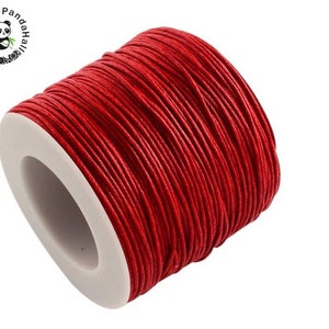 May include: A spool of red waxed cotton cord. The cord is wound tightly around a white plastic spool.