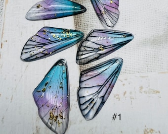 May include: Assortment of six iridescent blue and purple butterfly wing charms with gold glitter accents. #1