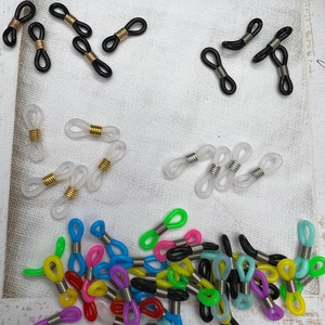 May include: Assortment of colorful plastic eyeglass chain connectors. The connectors are in various colors, including black, white, clear, pink, blue, green, and yellow. The connectors are designed to attach to eyeglass chains or cords.