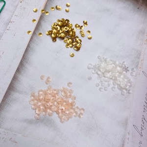 May include: Three piles of flower-shaped sequins in gold, white and peach.