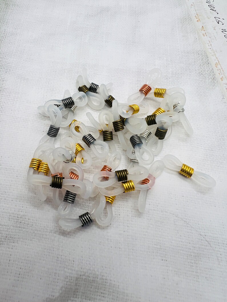 May include: A pile of clear plastic eyeglass chain holders with metal spring clips in gold, silver, copper, and black.