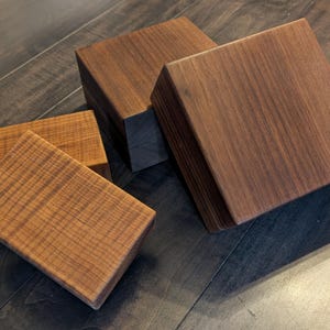 May include: Several wooden blocks with a rich, dark brown color and visible wood grain. The blocks are square or rectangular, with varying sizes. The wood has a natural, warm tone, and the blocks are arranged on a dark wooden surface.