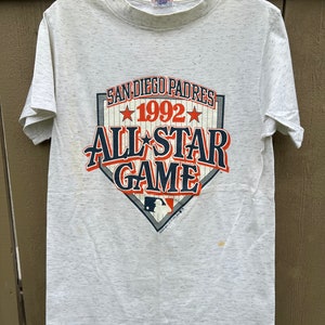May include: White t-shirt with a faded gray print of a baseball diamond with the text "San Diego Padres 1992 All-Star Game".