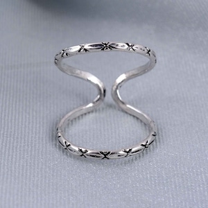 Könnte beinhalten: Ein silberner Ring mit einem Doppelband-Design. Der Ring hat ein dekoratives Muster aus kleinen Kreuzen an den Rändern.