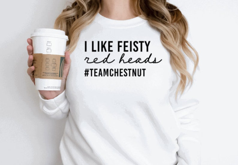 Może przedstawiać: Biała bluza z długim rękawem z czarnym napisem I LIKE FEISTY red heads #TEAMCHESTNUT. Odzież posiada okrągły dekolt i prosty kr&oacute;j, a napis wykonany jest przy użyciu kombinacji pogrubionych liter blokowych oraz czcionki imitującej pismo odręczne.