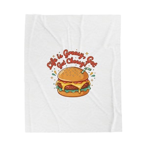 May include: White blanket featuring a cartoon burger with a straw. The burger has a sesame seed bun, cheese, and a patty. The text "Life is Greasy, Get Cheesy, Get" is written above the burger in red and orange.