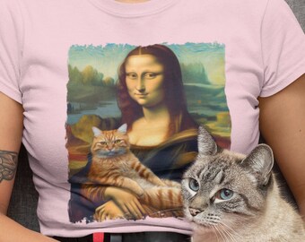 Peut inclure: Une femme portant un t-shirt rose avec un imprimé de la Joconde, mais avec un chat remplaçant sa main. Elle est assise sur un canapé gris et tient un chat sur ses genoux.