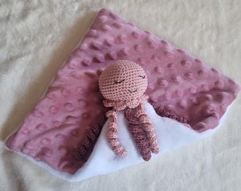 May include: A soft, triangular-shaped security blanket featuring a dusty rose-colored minky fabric with a raised dot texture on one side and a smooth white fabric on the other, topped with a small, crocheted light pink jellyfish toy.