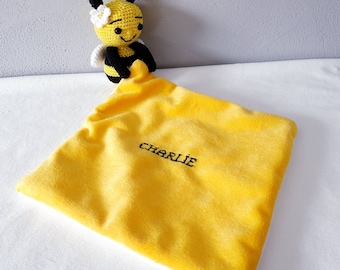 May include: A handmade yellow plush baby blanket with the name "CHARLIE" embroidered in black. A crocheted bee with black and yellow stripes, white wings, and a white flower is attached to the blanket.
