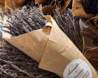 Op de afbeelding: Een gedroogd lavendelboeket verpakt in bruin papier met een ronde witte sticker met de tekst Lavender Missions Mentoring Teens Locally Helping Internationally. De gedroogde paarse bloemstelen zijn in een kegelvorm gebundeld.