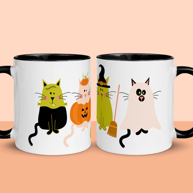 May include: Two white ceramic mugs with black rims. The mugs feature a Halloween theme with illustrations of cats dressed as a witch, a ghost, a pumpkin, and a Frankenstein monster.