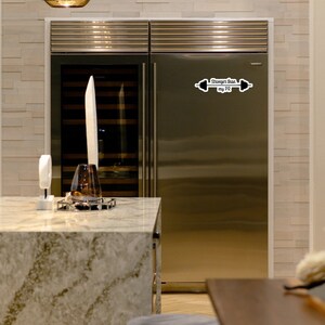 May include: A stainless steel refrigerator with a black and white sticker that says "Stronger than my PR" with a barbell graphic.