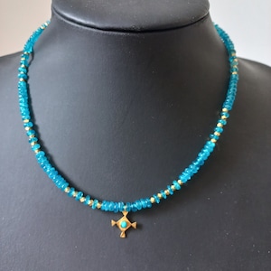 May include: A turquoise blue beaded necklace with a gold pendant featuring a turquoise stone in the center. The pendant is in the shape of a cross.