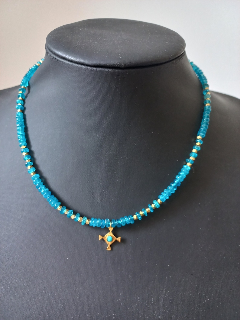 May include: A turquoise blue beaded necklace with a gold pendant featuring a turquoise stone in the center. The pendant is in the shape of a cross.