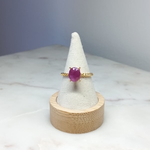 Peut inclure: Une bague en or avec une pierre ovale rose sertie au centre. La bague est sur un présentoir blanc.