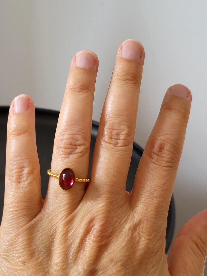 Puede incluir: Un anillo de oro con una piedra ovalada roja. El anillo est&aacute; en el dedo de una persona.