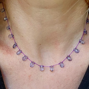 May include: A delicate necklace featuring teardrop-shaped, translucent purple beads strung on a thin, vibrant purple cord. The beads are evenly spaced, creating a minimalist and elegant design. This necklace is a piece of jewelry.