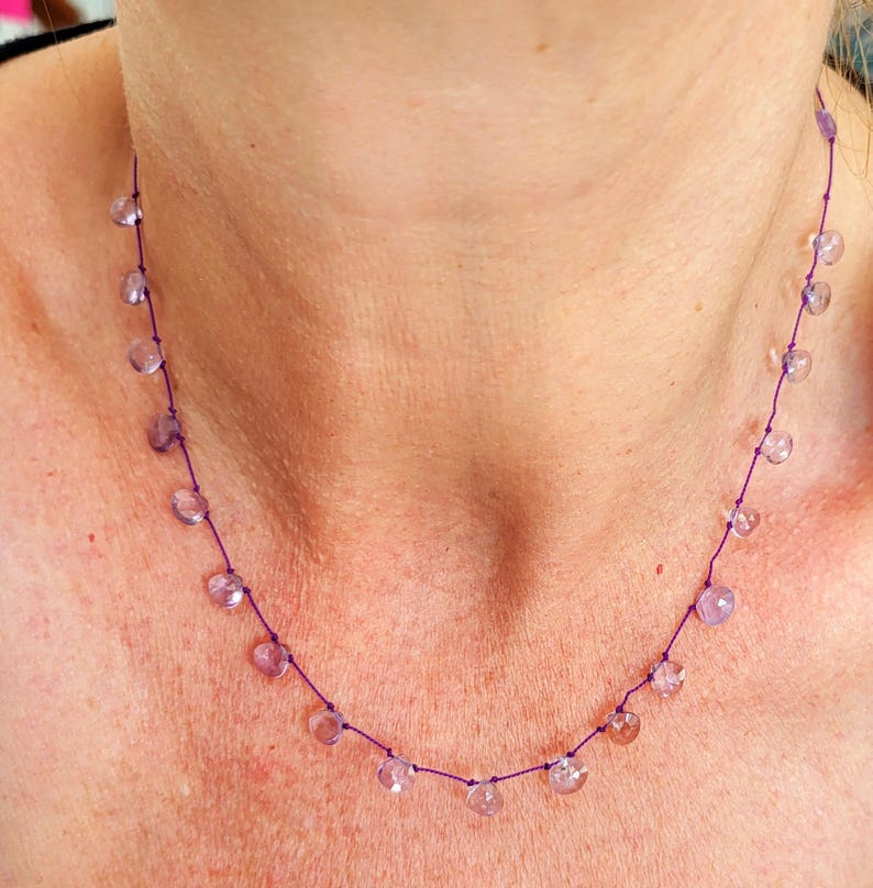Op de afbeelding: Een delicate ketting met een paarse koord en kleine, lichtpaarse edelsteen kralen.