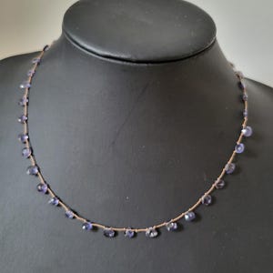 May include: A delicate necklace with a brown cord and small purple gemstones hanging from it.
