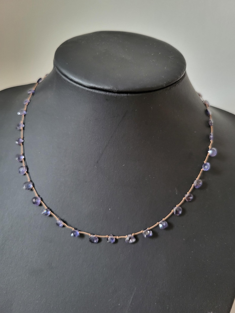 May include: A delicate necklace with a brown cord and small purple gemstones hanging from it.