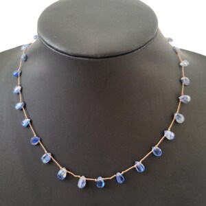 Puede incluir: Un collar delicado que presenta un cord&oacute;n fino de color marr&oacute;n claro ensartado con peque&ntilde;as piedras preciosas de cianita azul transl&uacute;cidas en forma de l&aacute;grima, espaciadas uniformemente a lo largo de toda la longitud de la cadena.