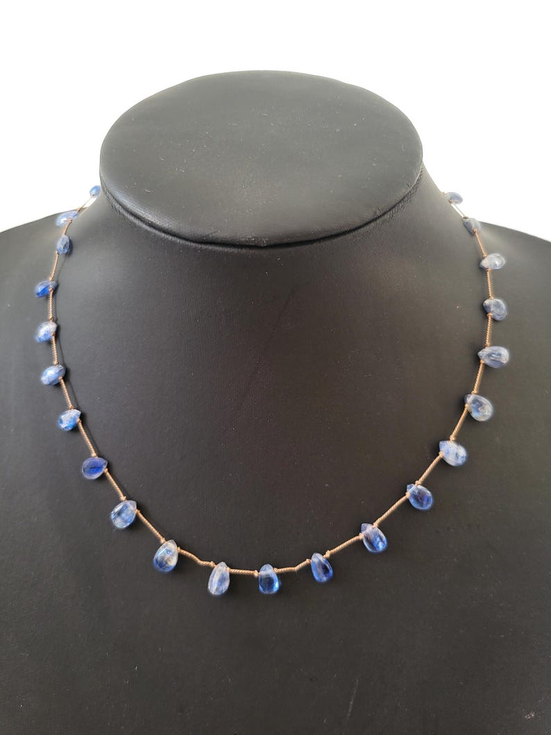 Puede incluir: Un collar delicado que presenta un cord&oacute;n fino de color marr&oacute;n claro ensartado con peque&ntilde;as piedras preciosas de cianita azul transl&uacute;cidas en forma de l&aacute;grima, espaciadas uniformemente a lo largo de toda la longitud de la cadena.
