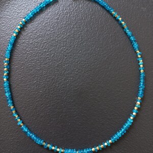 May include: A turquoise blue gemstone necklace with a gold pendant featuring a turquoise stone in the center. The pendant is in the shape of a cross with four points.