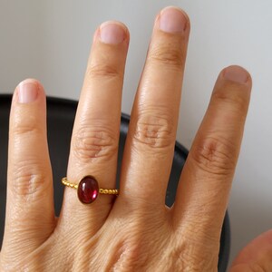 Puede incluir: Un anillo de oro con una piedra ovalada roja. El anillo est&aacute; en el dedo de una persona.