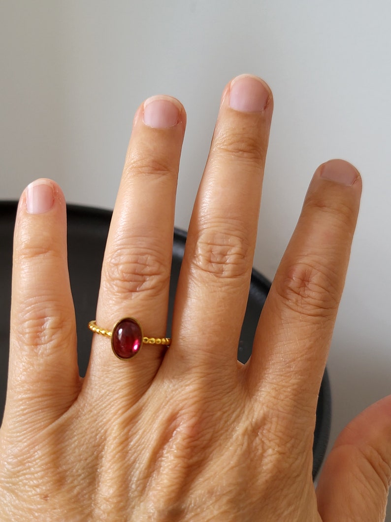 Puede incluir: Un anillo de oro con una piedra ovalada roja. El anillo est&aacute; en el dedo de una persona.
