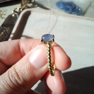 以下が含まれることがあります： 青い宝石が付いた金の指輪。指輪はねじれたバンドをしています。