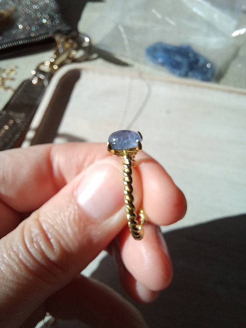 以下が含まれることがあります： 青い宝石が付いた金の指輪。指輪はねじれたバンドをしています。